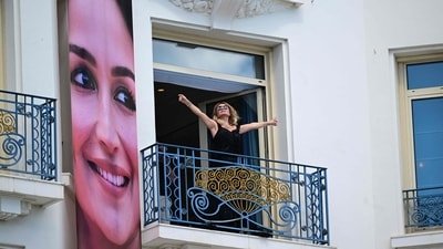 A woman gestures from the balcony of the Hotel Martinez, next to a poster of Bollywood star Alia Bhatt, on the eve of the start of the 79th edition of the Cannes Film Festival in Cannes, on May 11, 2026. (Photo by Olivier CHASSIGNOLE / AFP) (AFP)