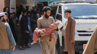 A man carries a child who was injured in the accident (Picture credit: AP) Journey home ends in tragedy: Truck carrying Afghan refugees from Pakistan overturns, killing 22