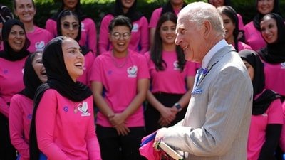 King Charles is presented with a hand decorated cricket bat from Shukria Noori during his meeting with members of the Afghan Refugee Women's Cricket Team at Clarence House on Wednesday. (AFP)