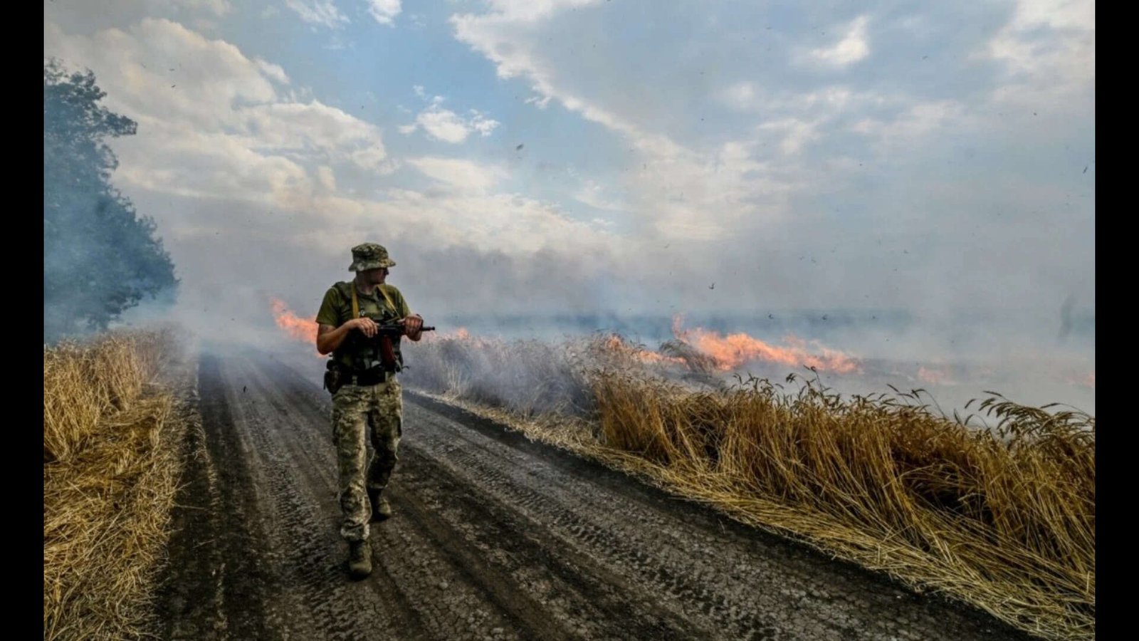 A Ukrainian fighter walks past a burning wheat field (Reuters file photo)