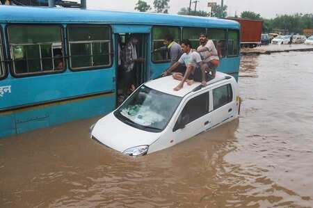 People taking refuge on a submerged car as vehicles ply on waterlogged road in Gurgaon