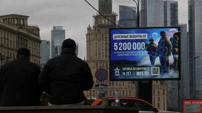 Men sit in front of an advertising board promoting military service under contract in the Russian Armed Forces and informing about payments, against the skyline of downtown Moscow, Russia ‘Dangerous path’: MEA urges Indians to stay away from Russian military recruitment